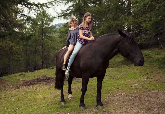女孩和女人坐在马背上horse in a forest.