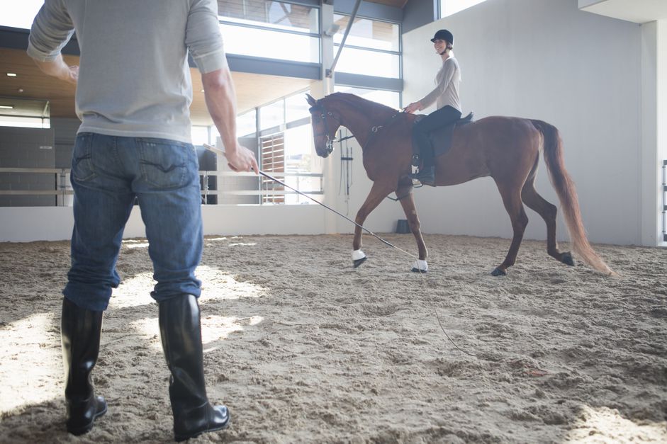 Female horseback riding with instructor in indoor paddock